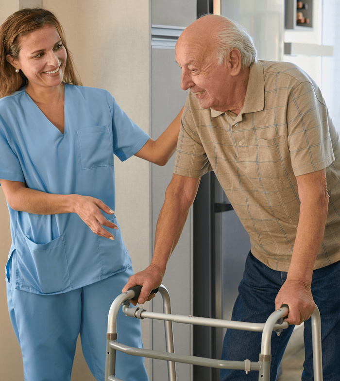 Caregiver assisting an elderly man using a walker at home, providing mobility support and daily living assistance.