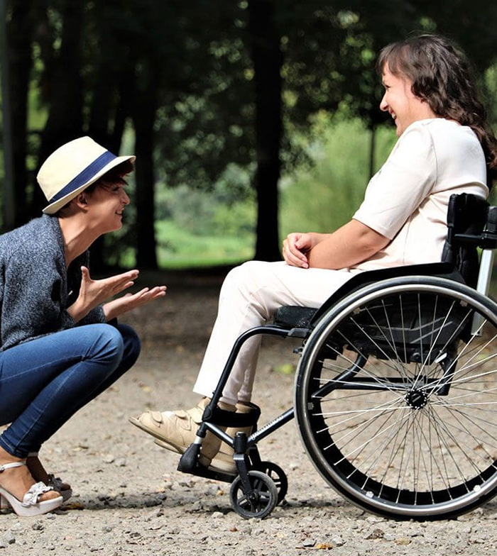 Support worker engaging in friendly conversation with a woman using a wheelchair in a park, promoting community participation and social connection.