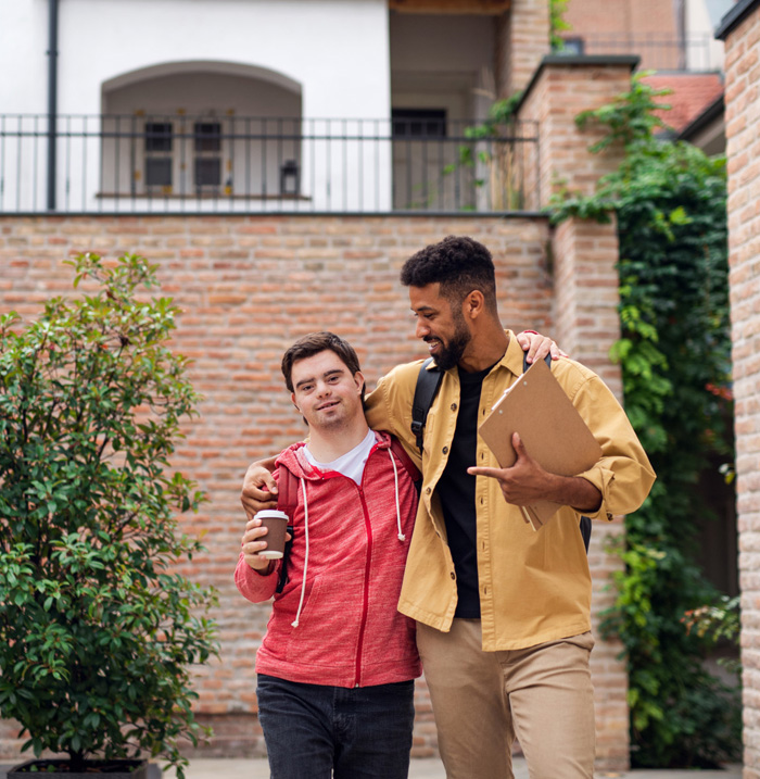 Support worker walking alongside a young man outdoors, offering community support and companionship as part of daily living assistance.