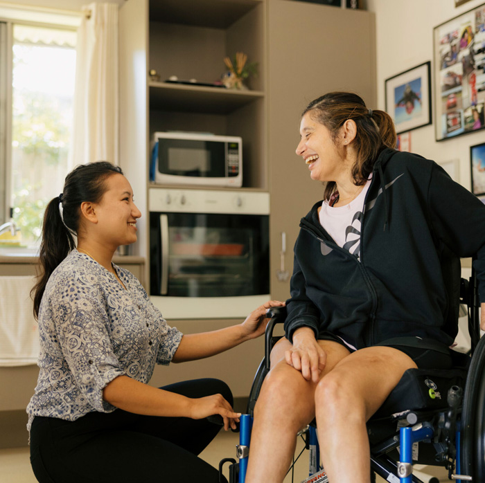 Caregiver assisting a woman in a wheelchair at home, providing personalised disability support and daily living assistance in a comfortable environment.