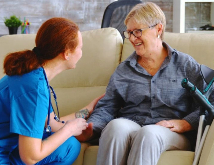 A caregiver and an elderly woman smiling and engaging in a positive interaction, promoting emotional support and well-being in a comfortable home environment.